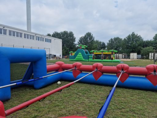 Aufblasbare Freizeitspielgeräte auf einer Wiese, darunter ein Spielplatz und ein Kickertisch.