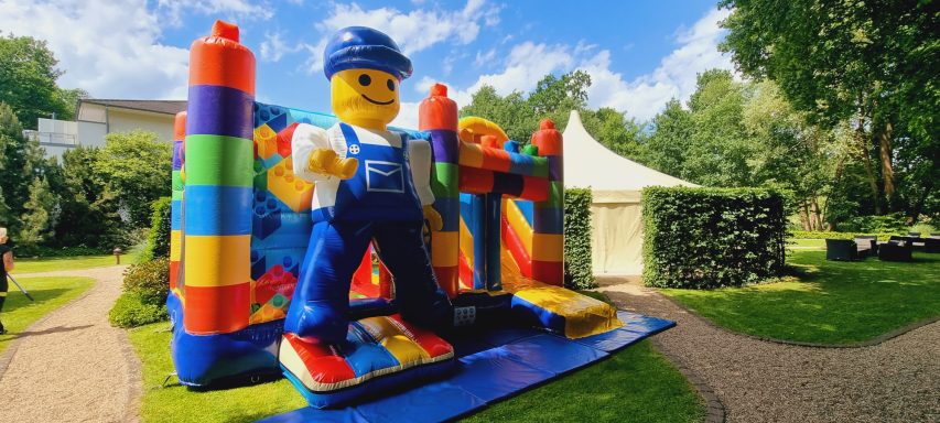 Bunte Hüpfburg mit einem großen LEGO-Männchen und einer Zelt-Umgebung im Freien.