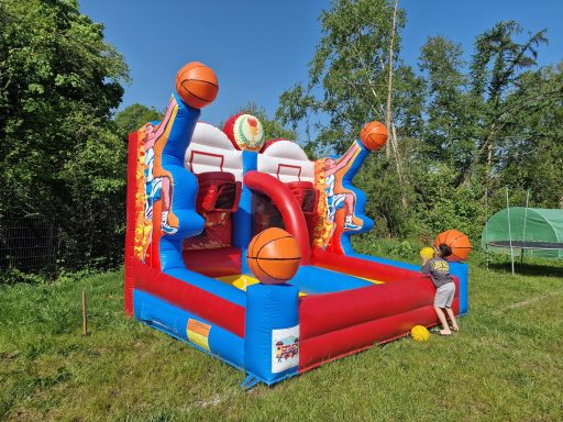 Sprungburg mit Basketballkörben und Bällen, ein Kind spielt damit im Freien.