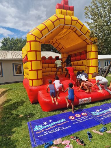 Kinder springen auf einer roten, palastähnlichen Hüpfburg im Freien.