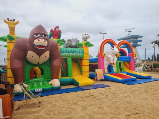 Luftige Hüpfburg mit einem großen Gorilla und bunten Rutschen am Sandstrand.