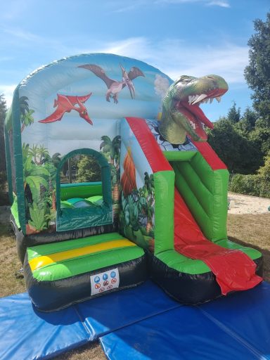 Bunte Hüpfburg im Dinosaurier-Thema mit Rutsche und einer Drachenkopf-Dekoration.