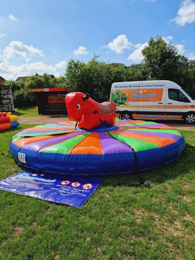 Buntes Rodeo-Bullen-Spielgerät auf einer Wiese mit einem Transportfahrzeug im Hintergrund.