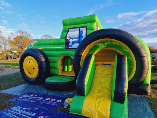 Bunte Hüpfburg in Form eines Traktors mit Rutsche auf einem Spielplatz.