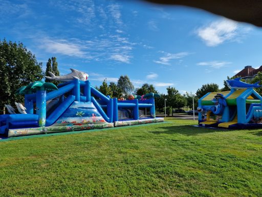 Bunte Hüpfburgen mit Rutschen auf einer grünen Wiese unter blauem Himmel.