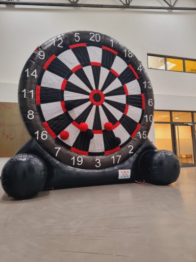 Große aufblasbare Dartscheibe mit roten und schwarzen Darts in einem Innenraum.