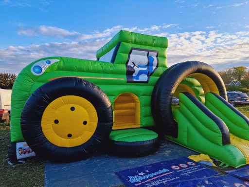 Buntes Trampolin in Form eines Traktors mit Rutsche und Zugang.