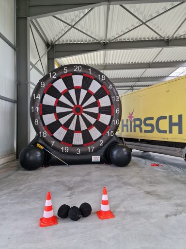 Großes aufblasbares Dartboard mit Darts vor einer Lagerhalle und zwei Warnkegeln.