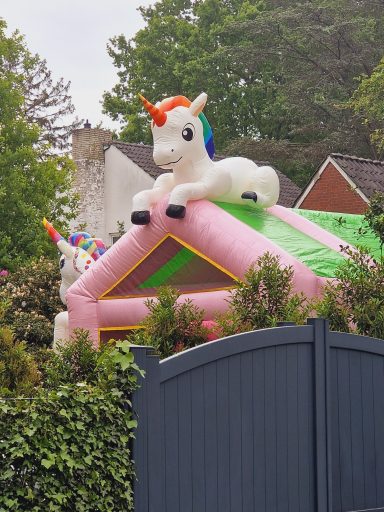 Buntes, aufblasbares Einhorn auf einem Spielhaus hinter einem Zaun.