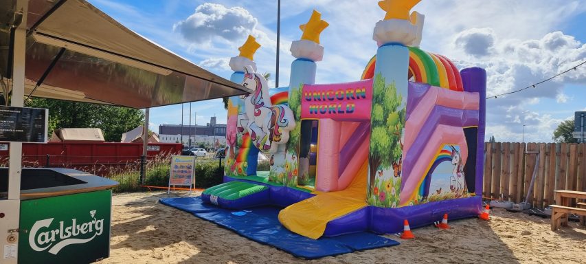 Buntes Hüpfburg mit Regenbogen und Einhornmotiv auf einem Spielplatz.