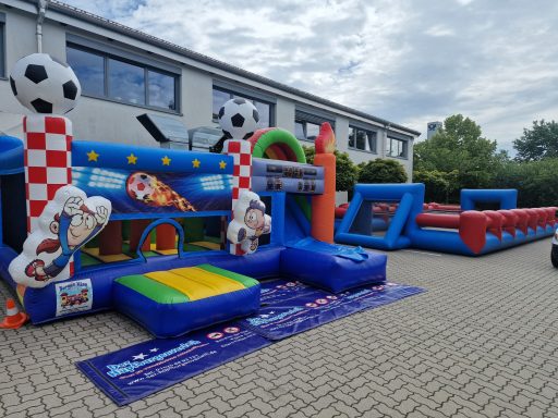 Aufblasbare Spielgeräte mit Fußballmotiven in einem Außenbereich auf gepflastertem Boden.