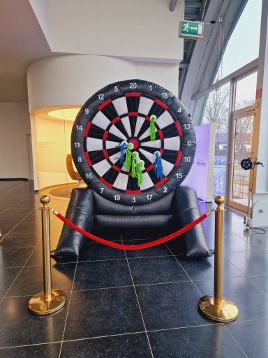 Ein aufblasendes Dartsboard mit bunten Darts, umgeben von Absperrseilen.