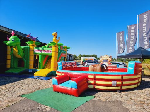 Bunte Hüpfburgen und ein aufblasbares Spielboot auf einem Festplatz bei Sonnenschein.