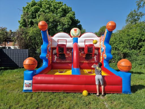 Bunte Hüpfburg mit Basketballkörben, auf der ein Kind spielt.