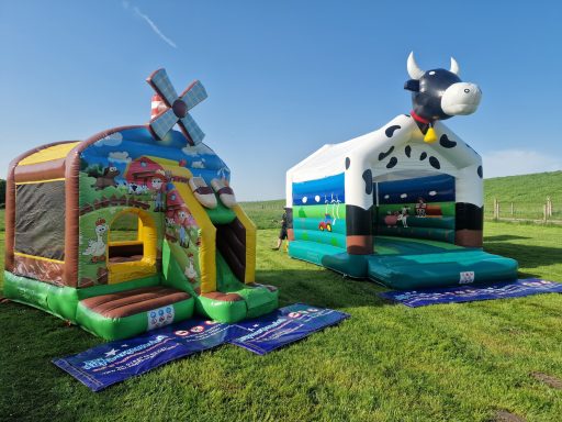 Bunte Hüpfburgen: eine mit Windmühle und eine mit Kuh-Design auf einer Wiese.