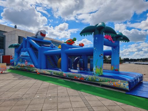 Bunte Wasserrutsche mit Palmen und spielerischen Elementen, auf einem Platz.