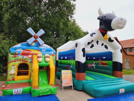 Buntes Trampolin mit Kuh-Design und Spielhaus in ländlicher Umgebung.