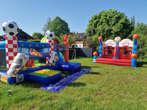 Bunte Hüpfburgen und Spielgeräte auf einer grünen Wiese im Freien.