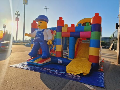 Bunte Hüpfburg mit Lego-Figur und Rutsche, im Freien bei Sonnenlicht.