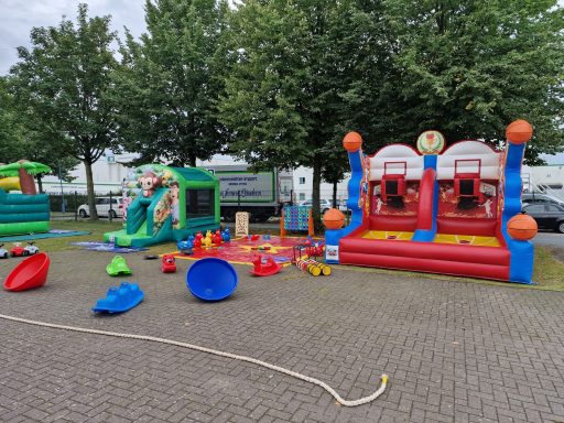 Buntes Spielplatzareal mit Hüpfburgen, Basketballkorb und Spielzeug im Freien.