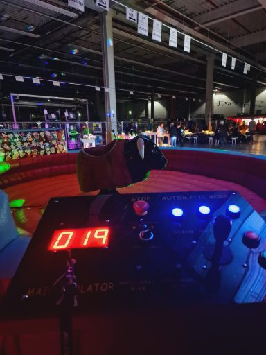 Controller mit digitaler Anzeige "019" in einer bunten Halle mit Menschen und Lichtern.