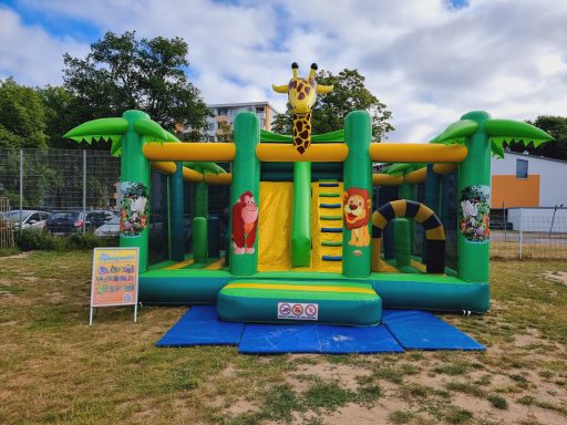 Bunte Hüpfburg mit Tieren, Rutsche und grünen Palmen im Freien.