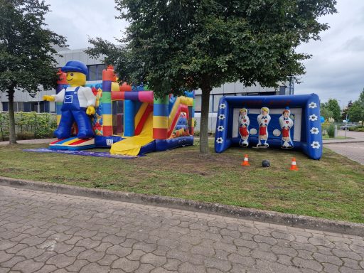 Bunte Hüpfburg mit Figuren und einer Rutsche, daneben ein Tor mit Sportfiguren.