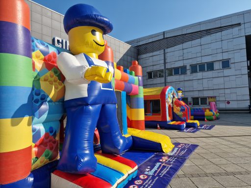 Bunte Hüpfburgen mit einem großen, lächelnden Lego-Männchen als Hauptfigur.