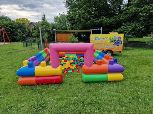 Bunte Hüpfburg mit farbigen Blöcken auf grünem Rasen in einem Spielplatz.