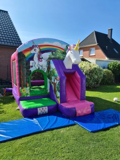 Bunte Luftburg mit Einhorn, Rutsche und Spielbereich im Garten.