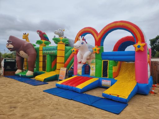 Bunte Hüpfburg mit Tieren und Rutschbahn auf einem sandigen Spielplatz.