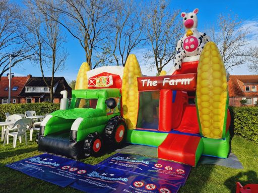 Bunte Hüpfburg im Bauernhof-Stil mit Traktor und einer Kuhfigur oben.