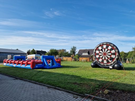 Auf einer Wiese stehen eine aufblasbare Spielstation und eine große Dartscheibe.