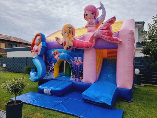 Bunte Hüpfburg mit Meerjungfrauenmotiven und Rutschen im Garten.