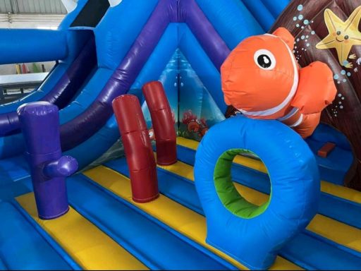 Buntes Hüpfburgen-Innenleben mit einem orangen Fisch-Kissen und farbigen Säulen.