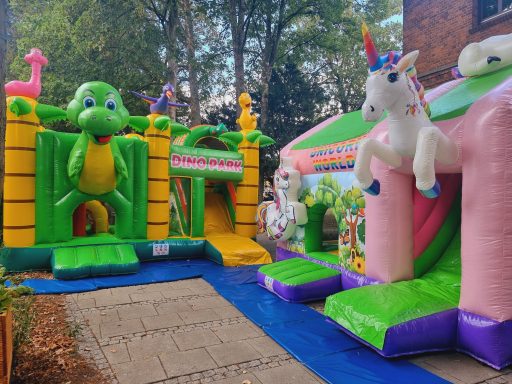 Bunte Hüpfburgen mit einem Dinosaurier und einem Einhorn in einem Garten.