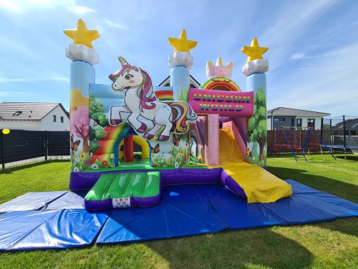 Buntes Hüpfburgen-Set mit Einhorn, Regenbogen und Rutsche auf grünem Rasen.