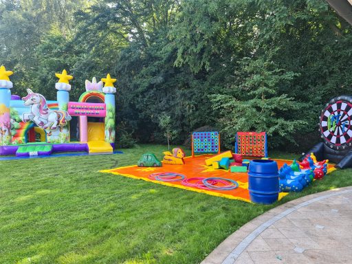 Bunte Spielbereiche mit Hüpfburg, Spielmatte und Zielscheibe im Garten.