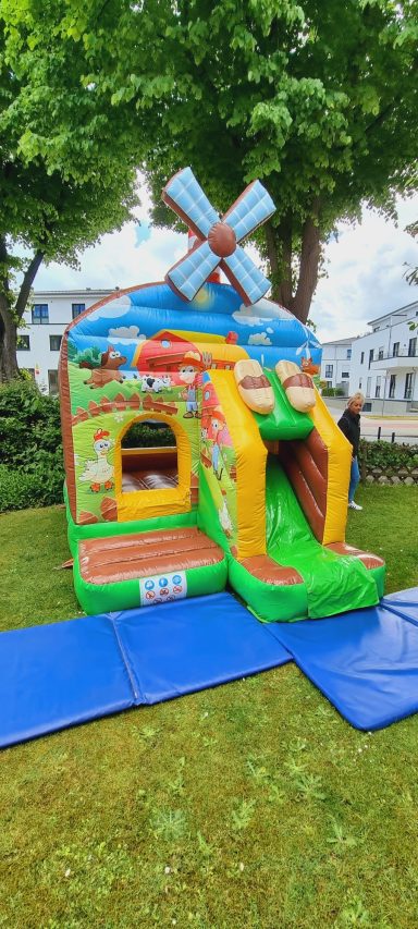 Bunte Hüpfburg mit Windmühle und Rutsche im Garten.