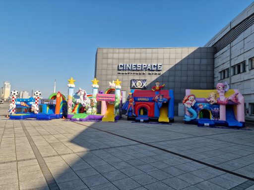 Bunte aufblasbare Spielgeräte stehen vor einem modernen Gebäude unter blauem Himmel.