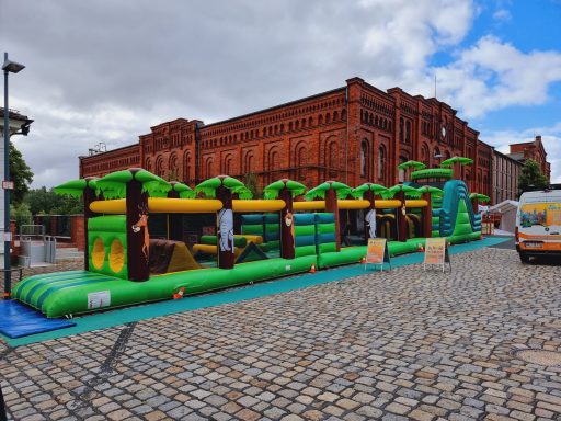 Buntes Hüpfburg-Set mit Palmen und Rutsche auf einem Kopfsteinpflasterplatz.