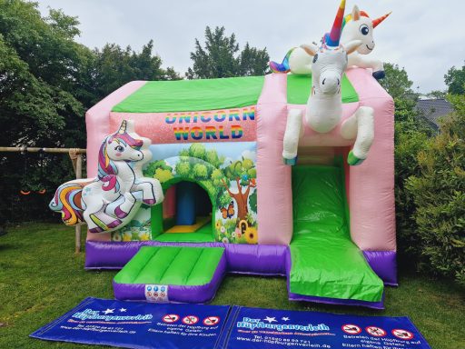 Bunte Hüpfburg mit Einhorn-Thema und Rutsche in einem Garten.