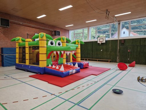 Aufblasbare Drachenrutsche mit grünen Palmen in einer Sporthalle.