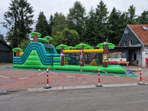 Bunte, aufblasbare Hüpfburg mit Palmen und mehreren Rutschen in einem Außenbereich.