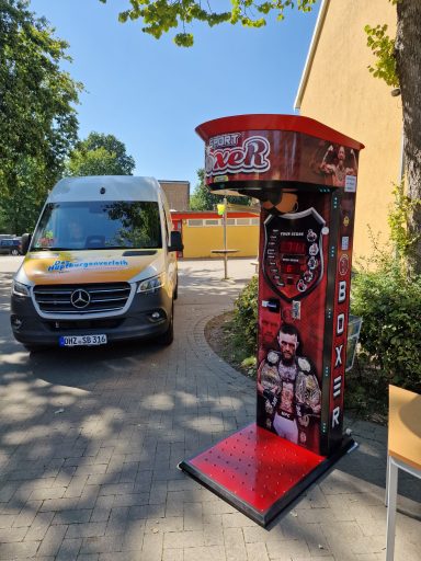 Rote Fotobox mit Grafiken von Wrestlern, vor einem Lieferwagen und einem Gebäude.