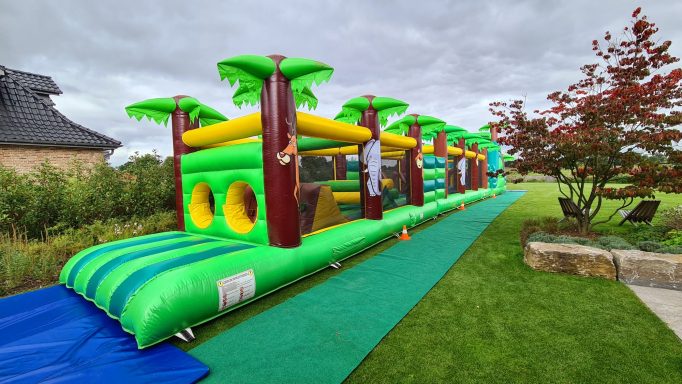 Bunte Hüpfburg mit Palmen, auf einer Wiese, für Kinder zum Spielen und Toben.