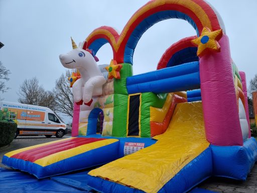 Buntes Hüpfburg mit Einhornmotiv und Rutsche in lebhaften Farben.