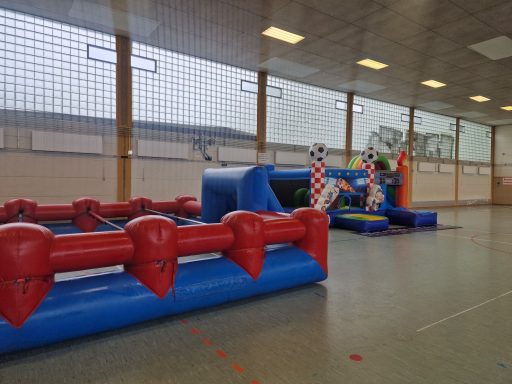 Bunte Hüpfburg und Spielgeräte in einer Sporthalle.